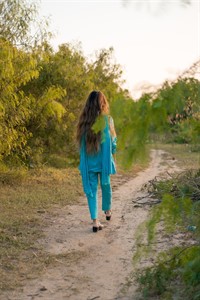 Girl in Pakistani dress walking on a path surrounded by greenery 