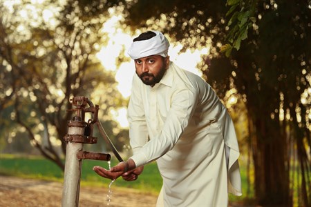 man in traditional clothes using a old water pump