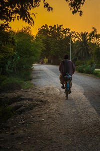 A man is riding bicycle on an empty road during sunset