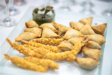 Fried breaded prawns and samosas on a plate with green sauce